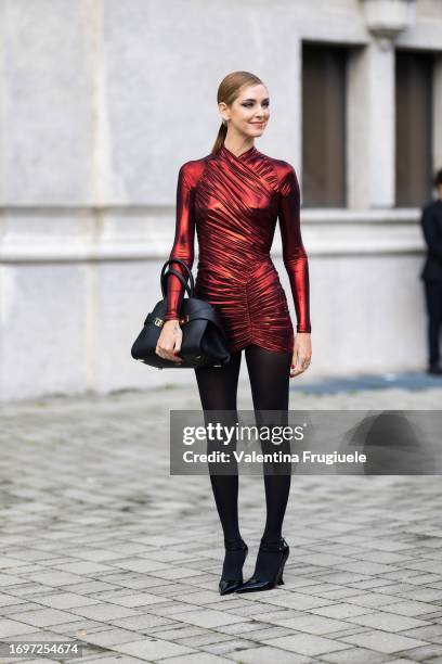 Chiara Ferragni is seen wearing blue eyeshadow, a red lycra long sleeves dress, black tights, black shiny pumps and a black leather Ferragamo bag...