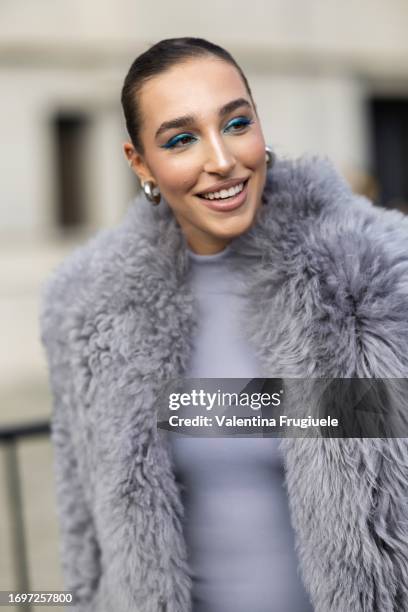 Ginevra Mavilla is seen wearing silver earrings, blue eyeshadow, a long grey long sleeves fur coat and a grey jumpsuit outside the Ferragamo show...