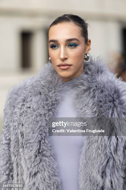 Ginevra Mavilla is seen wearing silver earrings, blue eyeshadow, a long grey long sleeves fur coat and a grey jumpsuit outside the Ferragamo show...