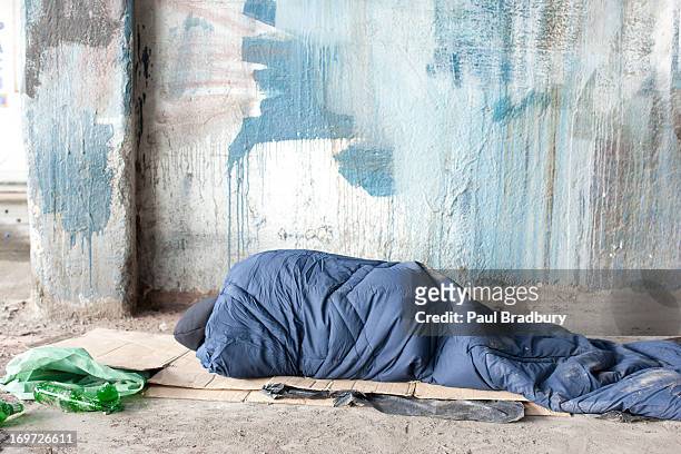 homeless man sleeping in sleeping bag on cardboard - homelessness stockfoto's en -beelden