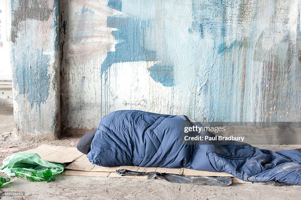 Homeless man sleeping in sleeping bag on cardboard