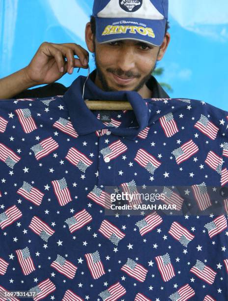 Vendor holds a T-shirt with the small images of the US flag printed all over it at a market in central Baghdad 28 May 2005. The T-shirt which sells...