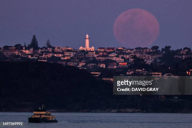 Ferry travels in front of a full moon, a supermoon also known as the "Harvest Moon", rising above Macquarie Lighthouse in Sydney on September 29,...