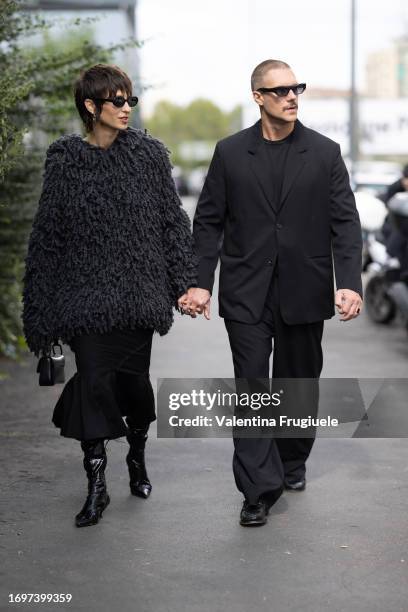 Marta Sanchez Castaneda is seen wearing black sunglasses, silver hoop earrings, a grey oversized poncho, black leather boots, a black long skirt and...