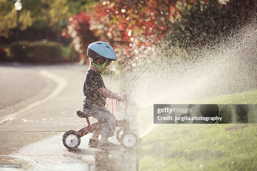 Child on tricycle playing in the sprinkler