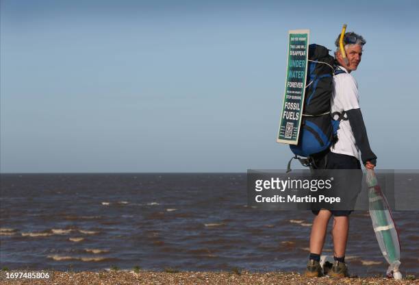 Dr Charlie Gardner wears a sign on his backpack warning of the danger of rising sea levels on the north Norfolk coast during a walk to highlight...