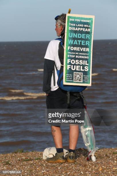 Dr Charlie Gardner wears a sign on his backpack warning of the danger of rising sea levels as he takes moment to look out to sea during a walk to...