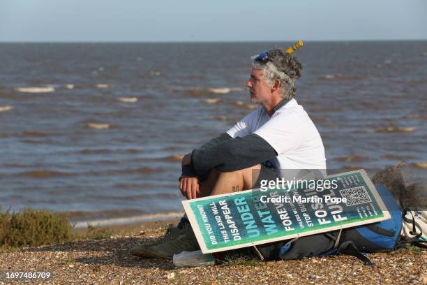 Dr Charlie Gardner sits and looks out to sea alongside a sign warning of the danger of rising sea levels during a walk to highlight climate change on...