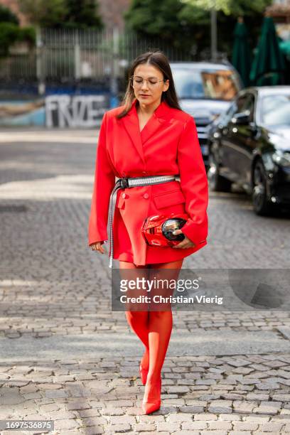 Guest wears red car bag, belt, red blazer, tights outside Ferrari during the Milan Fashion Week - Womenswear Spring/Summer 2024 on September 23, 2023...
