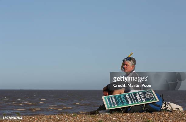 Dr Charlie Gardner sits and looks out to sea alongside a sign warning of the danger of rising sea levels during a walk to highlight climate change on...