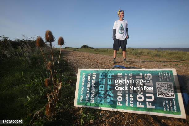 Dr Charlie Gardner stands and takes in his environment behind a sign warning of the danger of rising sea levels as he takes moment to look out to sea...