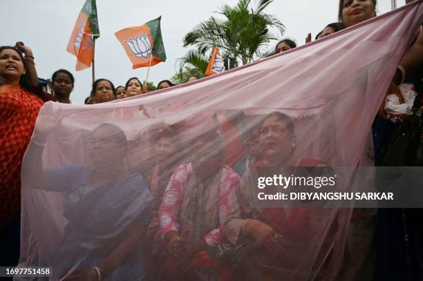 Activists of the women wing of the Bharatiya Janata Party sit under a mosquito net during a protest against the authorities' failure to control the...