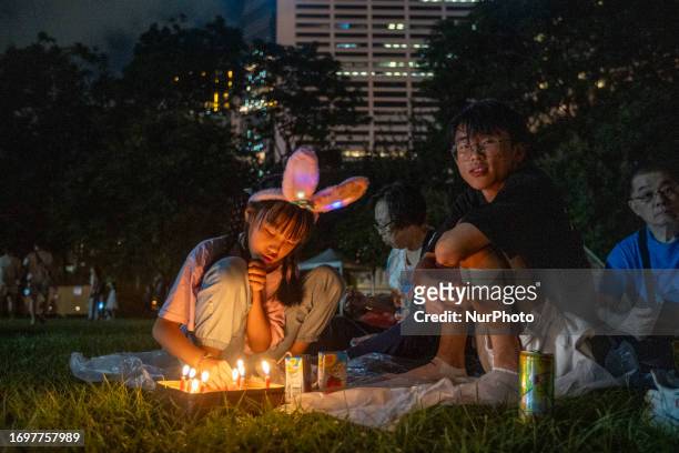 Girl sitting on the grass looking at burning candles at Victoria Park on September 29, 2023 in Hong Kong, China. Today marks the Mid Autumn Festival.
