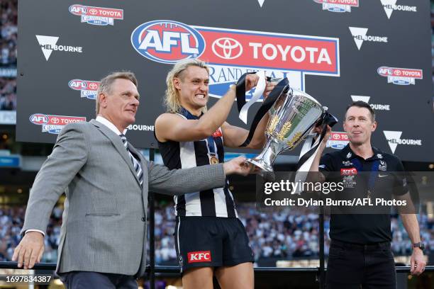 Peter Moore, Darcy Moore of the Magpies and Craig McRae, Senior Coach of the Magpies lift up the premiership cup during the 2023 AFL Grand Final...