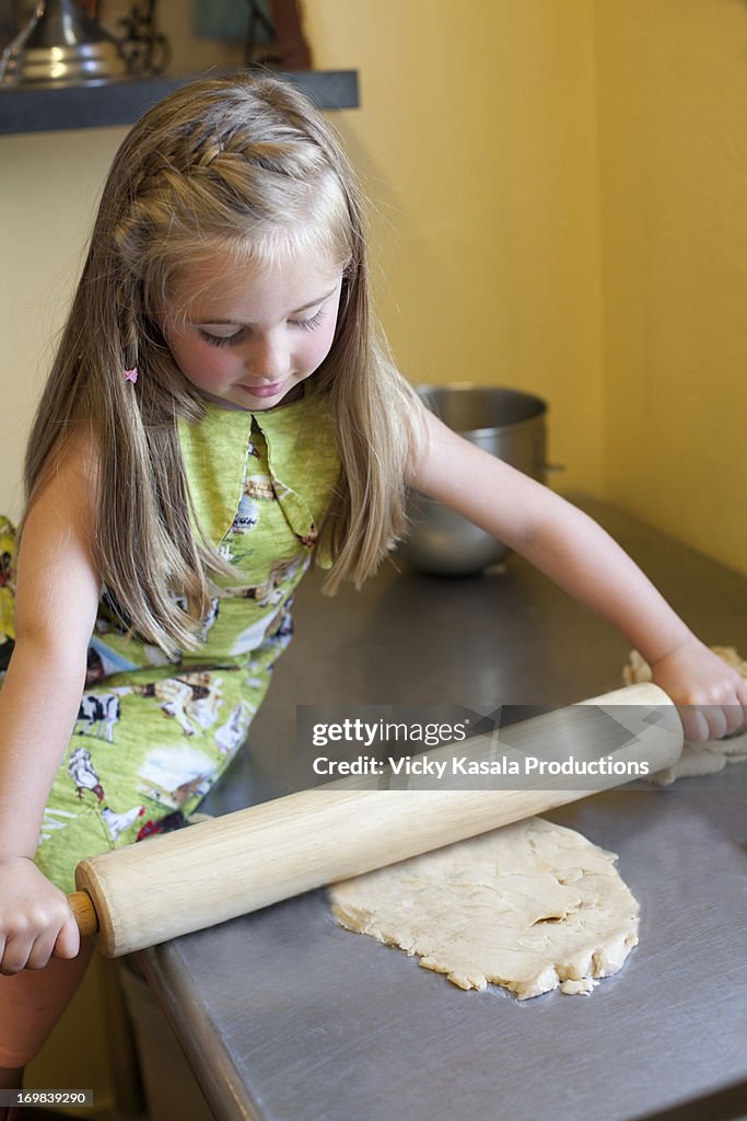 Young girl rolling pie dough in kitchen.