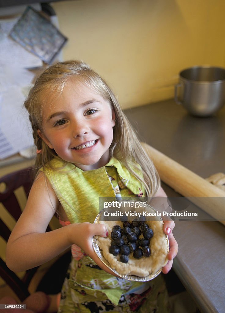 Young girl holding pie that she made in kitchen.