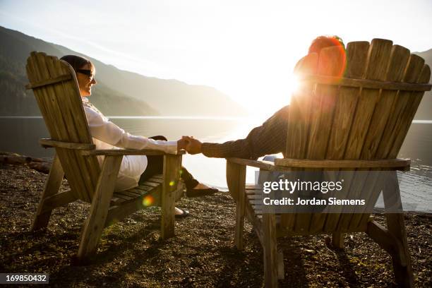 an older couple relaxing near a lake. - adirondack chair stock pictures, royalty-free photos & images