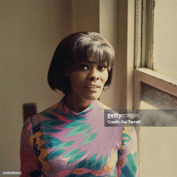 American singer Dionne Warwick wearing a multi-coloured outfit, poses beside a closed window, ahead of performing at the Newport Jazz Festival in...