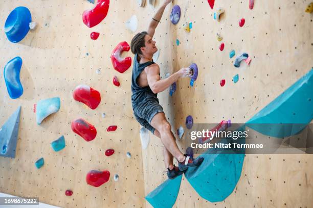 indoors bouldering is good for treating your mental health issues. full length of a climber bouldering at an indoor climbing wall. - emotional intelligence stock pictures, royalty-free photos & images