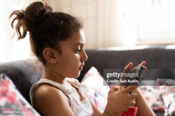 young girl lying on sofa looking at smartphone. - kurdish girl stock pictures, royalty-free photos & images