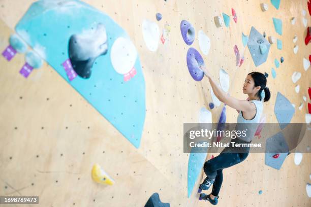 sport climbing brings a level of success for your goals. a asian female climber scaling and gripping on an artificial boulder wall in an indoor rock climbing gym. - bouldering stock pictures, royalty-free photos & images