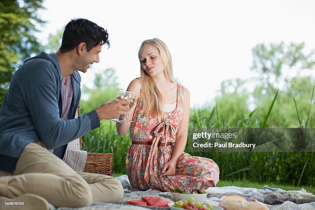 Casal Jovem picnicking e copos de torrar Vinho no parque