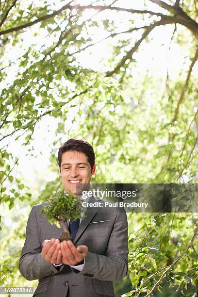 homme d'affaires tenant plante en plein air - homme costume jardinier photos et images de collection