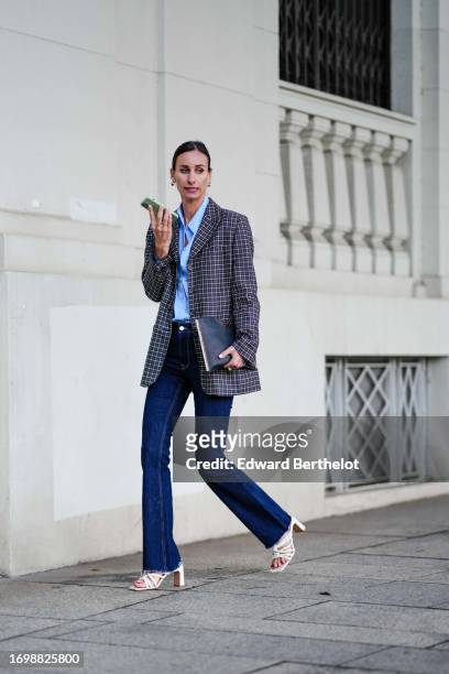 Guest wears a checkered oversized blazer jacket, a blue shirt, blue flared denim jeans, white high heels shoes, outside The Attico, during the Milan...