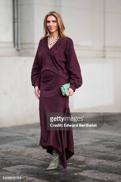 Guest wears a purple / burgundy v-neck pullover with puff sleeves, a matching gathered midi skirt, pointed leather khaki boots, outside The Attico,...