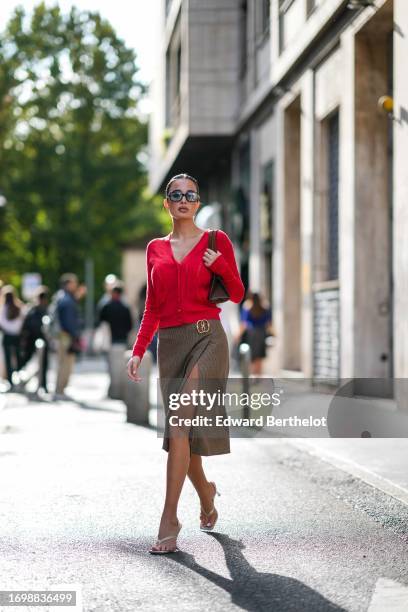 Guest wears sunglasses, a red cardigan , a Gucci detail, a short on-knee slit brown skirt, white kitten heels shoes, outside Bally, during the Milan...