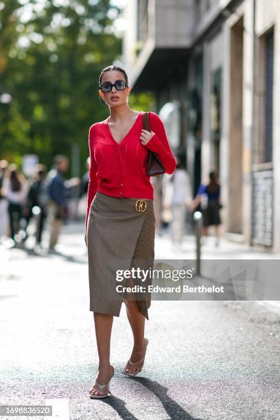 Guest wears sunglasses, a red cardigan , a Gucci detail, a short on-knee slit brown skirt, white kitten heels shoes, outside Bally, during the Milan...