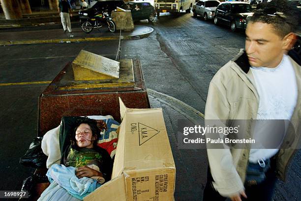 Man walks past a homeless women sleeping on the street December 22, 2002 in Caracas, Venezuela. Approximately 80% of the people live in poverty in...