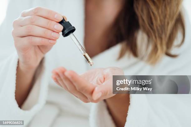 woman drips cosmetic oil onto her palm to massage her scalp and improve the quality and beauty of her hair. - pipeta imagens e fotografias de stock