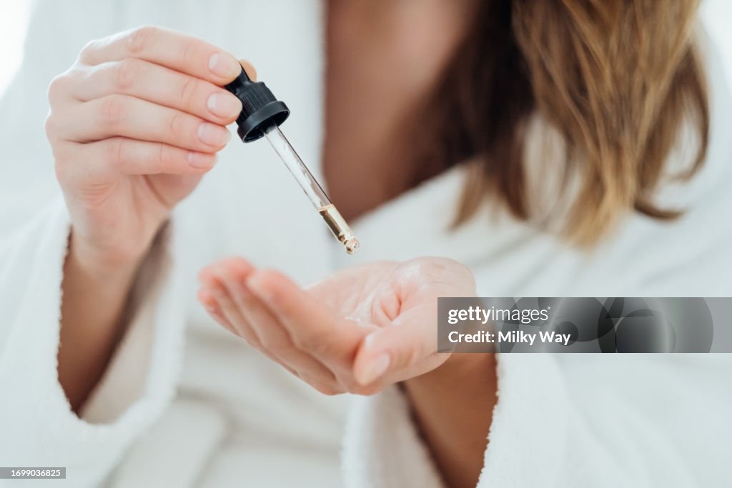 Woman drips cosmetic oil onto her palm to massage her scalp and improve the quality and beauty of her hair.