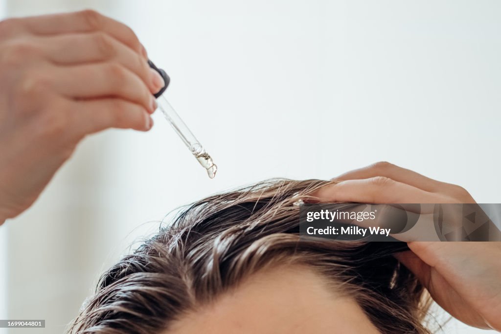 Woman applies oil to her hair with pipette. Beauty caring for scalp and hair.