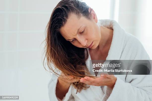 blond woman examines the split ends on her dry and damaged hair, highlighting the concept of at-home hair care treatment. - damaged hair stock pictures, royalty-free photos & images