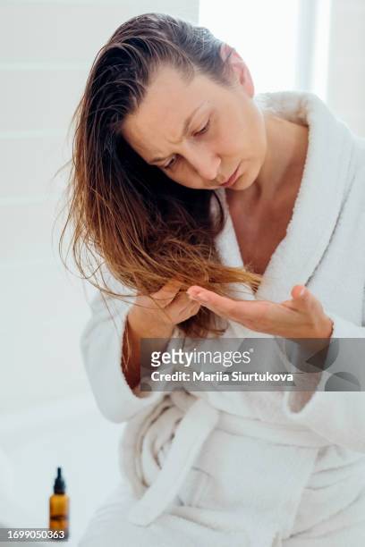 young woman assesses the split ends in her dry and damaged hair, emphasizing the idea of home-based hair care treatment. - examining hair stock pictures, royalty-free photos & images