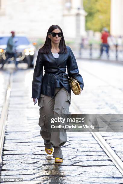 Guest wears black belted jacket, grey pants with side pockets, golden Bottega Veneta bag outside The Attico during the Milan Fashion Week -...