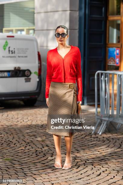 Guest wears red cardigan, beige skirt with slit, brown bag outside Bally during the Milan Fashion Week - Womenswear Spring/Summer 2024 on September...