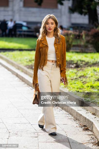 Guest wears brown jacket with fringes, creme white pants, bag outside Bally during the Milan Fashion Week - Womenswear Spring/Summer 2024 on...