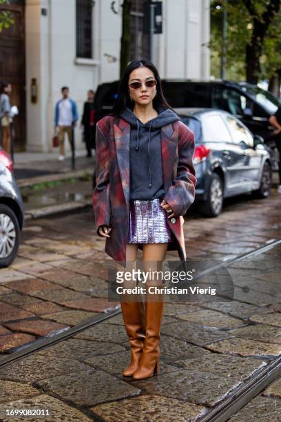 Yoyo Cao wears grey hoody, oversized blazer, silver mini skirt, brown boots outside The Attico during the Milan Fashion Week - Womenswear...