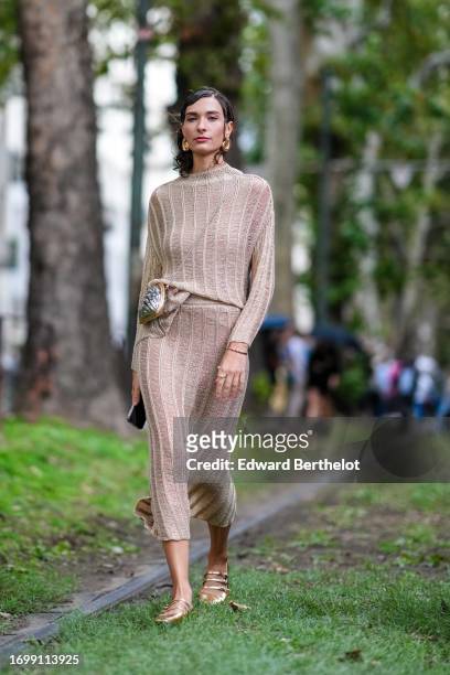 Guest wears golden earrings, a beige wool knit long dress, a silver shell shaped bag, outside Dolce & Gabbana, during the Milan Fashion Week -...