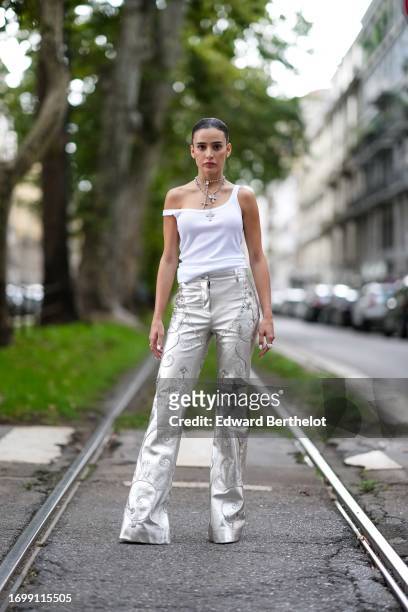 Guest wears cross-shaped necklaces, a white tank top, bejeweled silver flared long pants, outside Dolce & Gabbana, during the Milan Fashion Week -...
