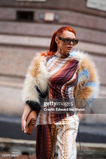 Guest wears sunglasses, a fluffy colored jacket, a gathered turtleneck colored top with geometric patterns, flared pants, a brown leather bag,...