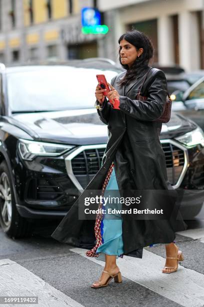 Guest wears a black leather long coat, blue flowing skirt, outside Dolce & Gabbana, during the Milan Fashion Week - Womenswear Spring/Summer 2024 on...