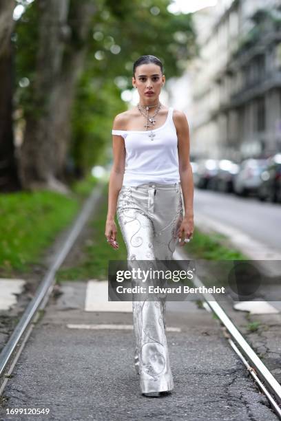 Guest wears cross-shaped necklaces, a white tank top, bejeweled silver flared long pants, outside Dolce & Gabbana, during the Milan Fashion Week -...