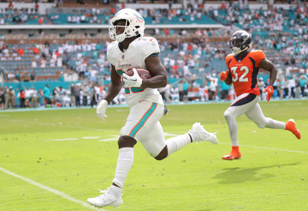 De'Von Achane of the Miami Dolphins runs past Delarrin Turner-Yell of the Denver Broncos while scoring a rushing touchdown during the fourth quarter...