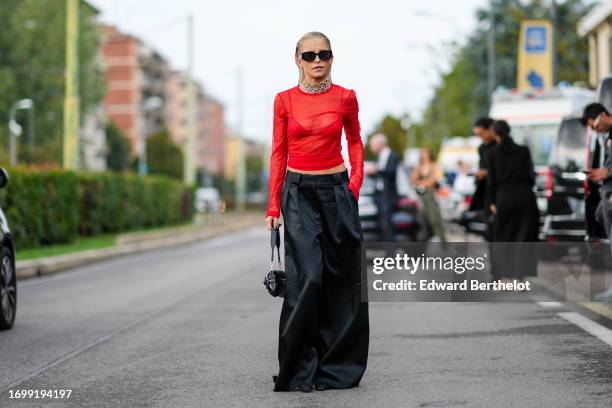 Caroline Daur wears sunglasses, multiple chains necklace / choker, a red mesh crop top, red bras, a black leather puff quilted bag, black lustrous...