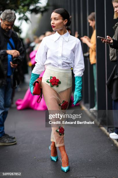 Guest wears a white shirt, a red leather bag, beige underwear, a mesh midi skirt with floral red details, fishnet tights, blue shiny / turquoise...