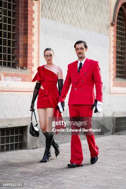 Guest wears sunglasses, a piercing, long black gloves, a red one-shoulder mini dress, a black bag, black pointy under-the-knee high-heeled Balenciaga...